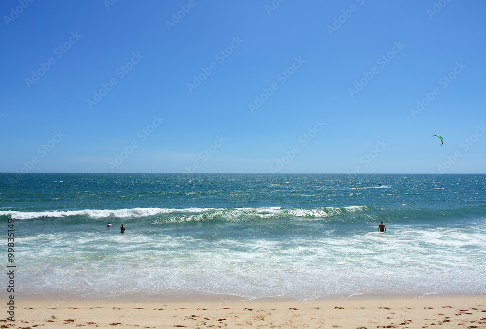 People swim and play in the sea, sandy beach and clear blue sky;