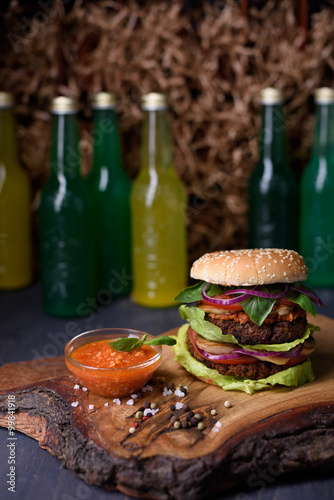 Fresh homemade burger on wooden serving board with lemonade, spicy tomato sauce, sea salt and herbs.