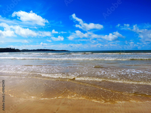 Calm tropical beach with white sand and turquoise water under blue cloudy sky