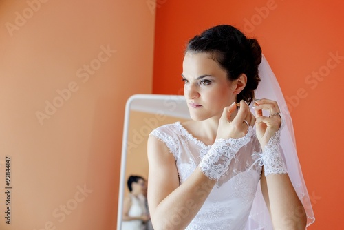 Beautiful bride in white wedding dress puts on earring.