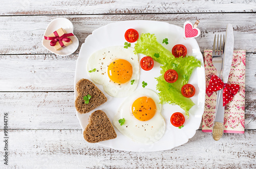 Breakfast on Valentine's Day - fried eggs and bread in the shape of a heart and fresh vegetables. Top view