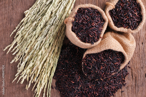 Riceberry rice in small burlap sack and ear of rice on wooden table.