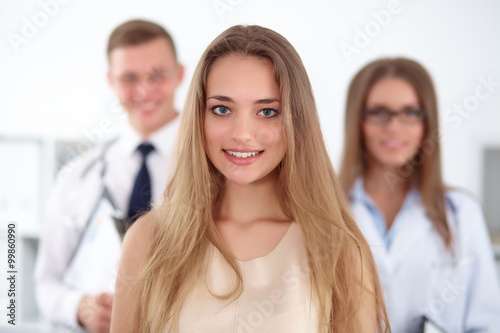 Happy smiling female patient with two cheerful doctors in the background. Medical and health care concept