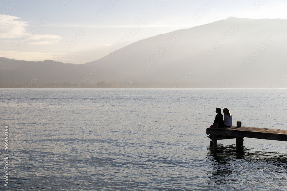 Personnes assises sur un ponton en bois regardant l'horizon d'un lac Personnes assises sur un ponton en bois regardant l'horizon d'un lac