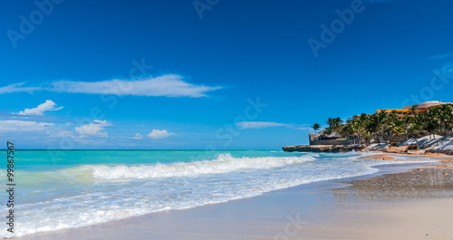 Warm ocean waves gently lap against a Cuban beach.  Cloudscape on horizon with waves gently breaking on the shore. 