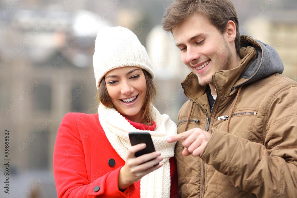 Couple consulting a smart phone in winter Couple consulting a smart phone in winter