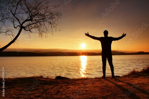 Lone sportsman looking at colorful sunset on shore of autumn lake