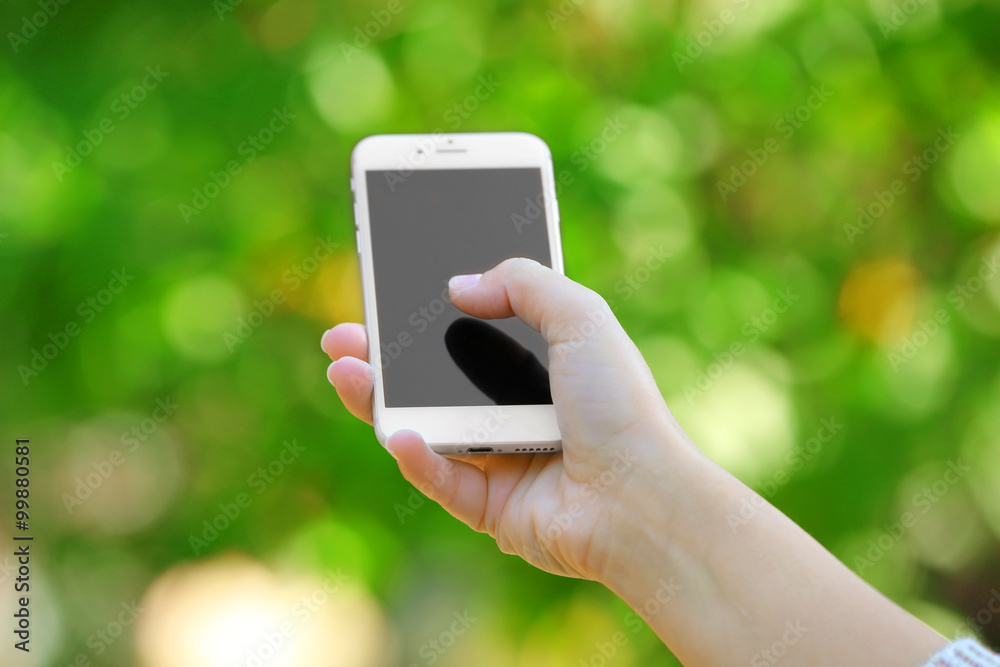 A female hand holding a mobile phone outdoors, on blurred background