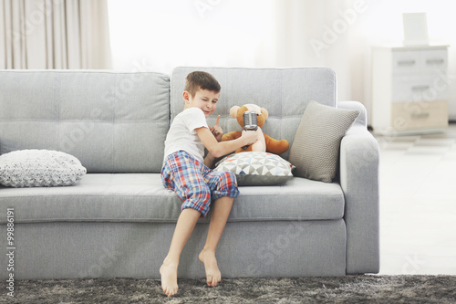 Little boy with Teddy bear singing with a microphone on a sofa at home