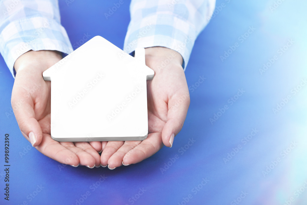 Female hands holding house on blue background Female hands holding house on blue background