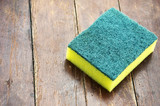 Dishwashing sponge with a wooden floor in the background.