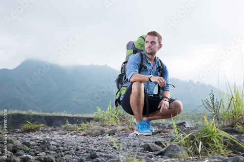 Handsome young caucasian man sitting on hood of a jeep, mountain