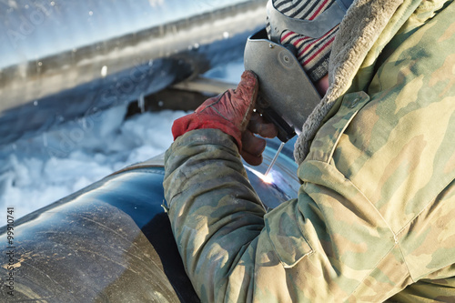 welder performs welding pipeline in winter conditions