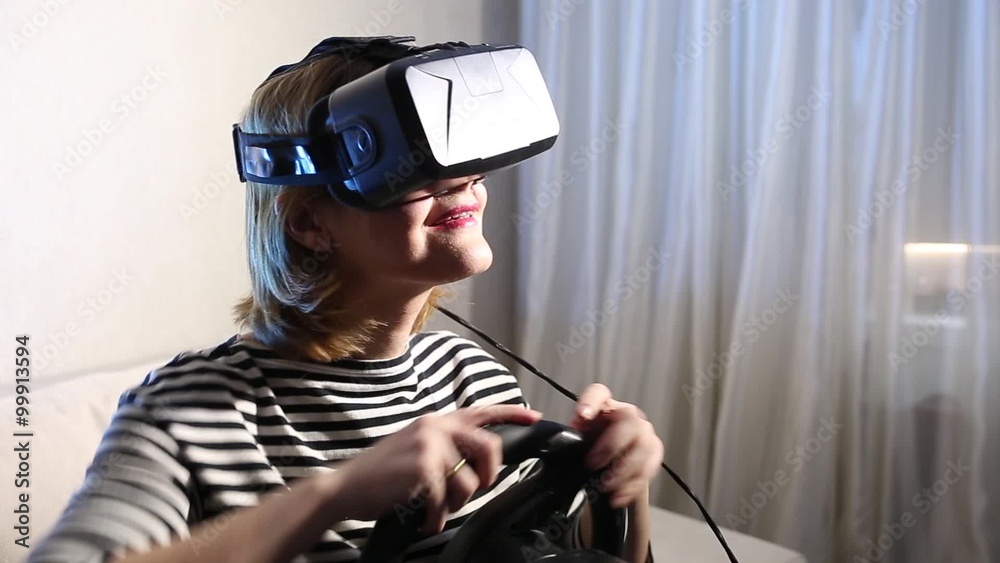 happy smiling young beautiful girl holding a gaming computer wheel getting experience using VR-headset glasses of virtual reality at home happy smiling young beautiful girl holding a gaming computer wheel getting experience using VR-headset glasses of virtual reality at home