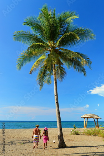 Couple walking on the tropical sandy beach with palm trees