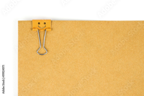 Orange happy face paperclip nipped at brown paper on white background. 