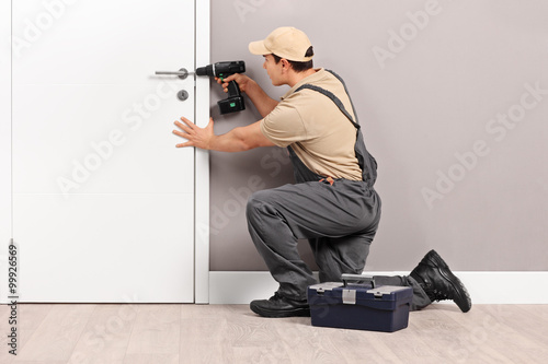 Young locksmith installing a lock on a door photo