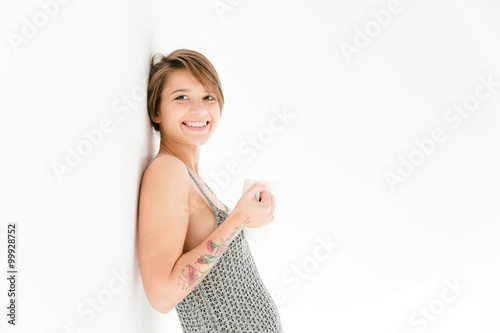 Photos Happy cheerful young woman leaning the wall and drinking tea