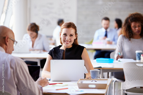 Portrait Of Businesswoman Working On Laptop In Busy Office