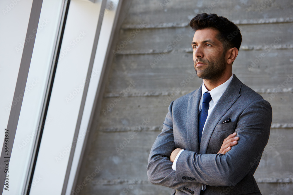 Hispanic Businessman Standing Against Wall In Modern Office Hispanic Businessman Standing Against Wall In Modern Office