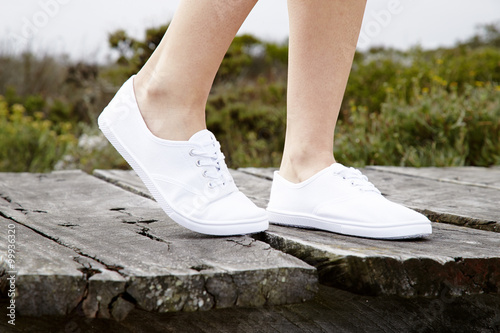 White sneakers on model walking on boardwalk, close up