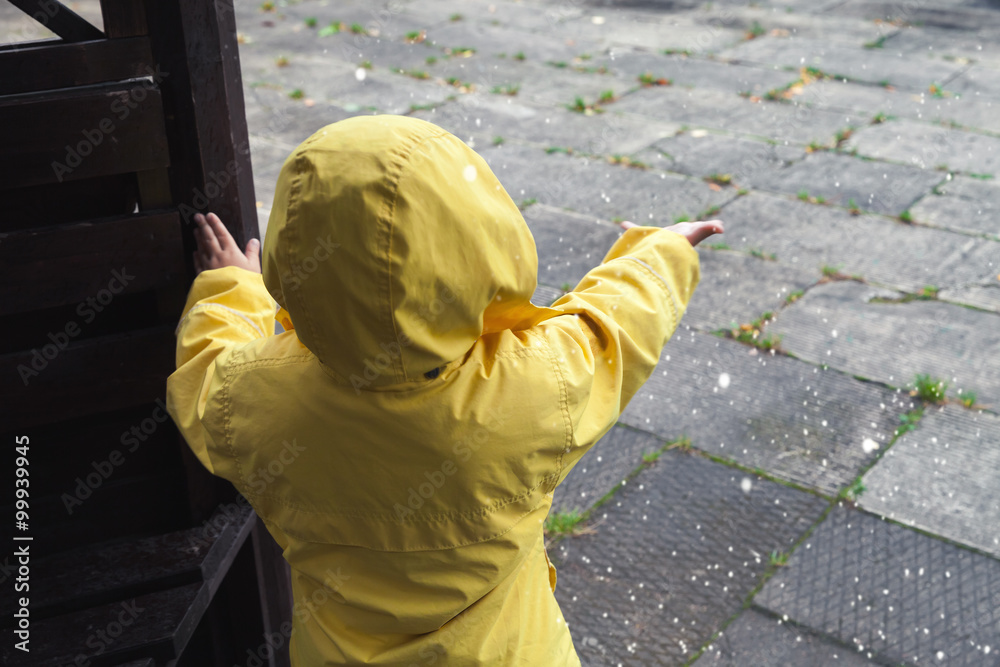 Little child in raincoat playing with water drops