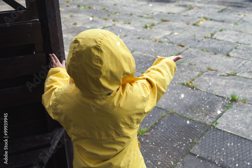 Little child in raincoat playing with water drops