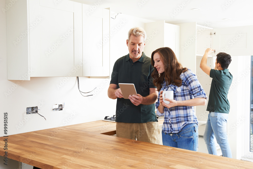 Woman With Carpenter Looking At Plans For Kitchen On Digital Tab Woman With Carpenter Looking At Plans For Kitchen On Digital Tab