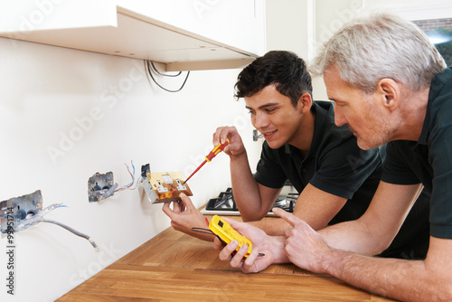 Electrician With Apprentice Working In New Home