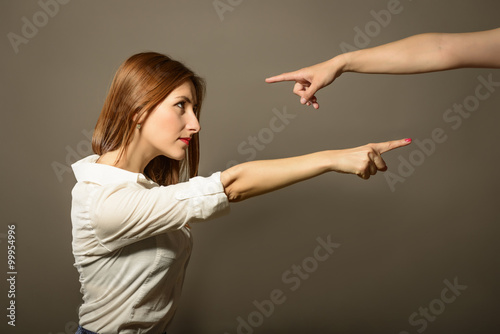 Beautiful woman point finger on someone while someone else pointing finger on her, studio shot on gray background. Side profile portrait of angry upset person, blaming other. Negative human emotion photo