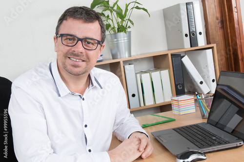 Man, wearing glasses and smiling, as he works on laptop