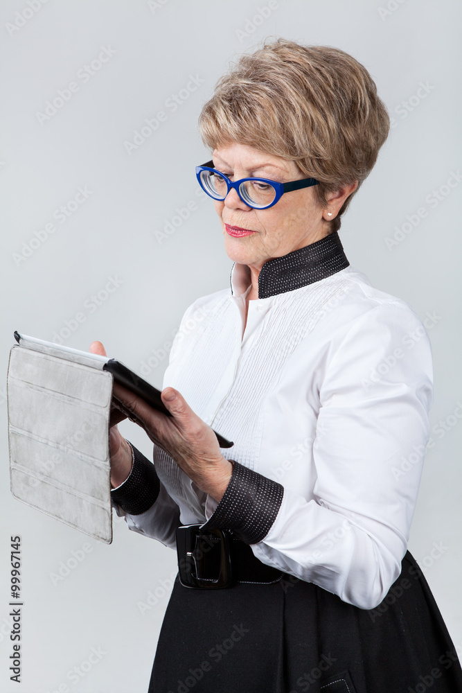 Senior Caucasian woman reading message at the tablet screen, grey background