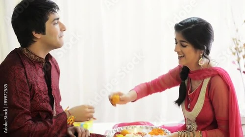 Pan shot of a teenage girl feeding sweet to her brother at Raksha Bhandan festival photo