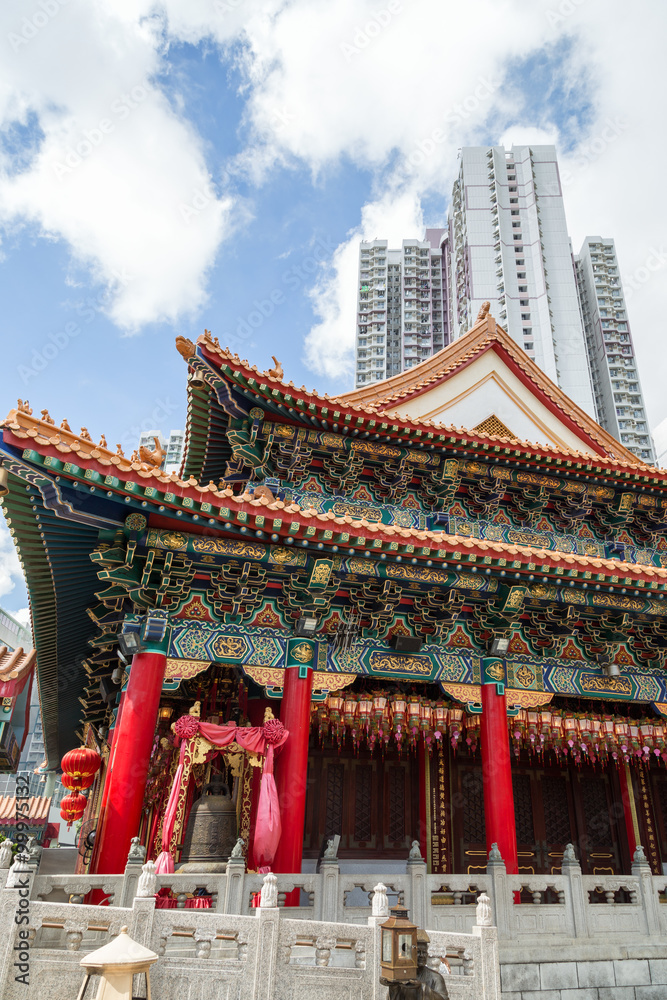Ornate Sik Sik Yuen Wong Tai Sin Temple and skyscraper behind it in Hong Kong, China.