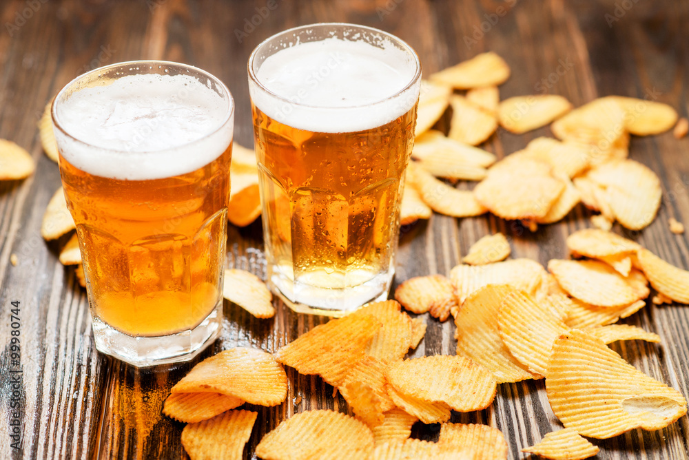 Light foamy beer with potato chips on a wooden background Light foamy beer with potato chips on a wooden background