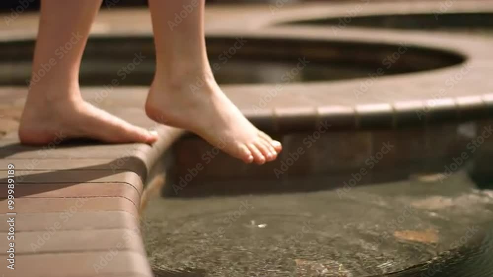 A woman testing the water in a pool with her toes, in slow motion