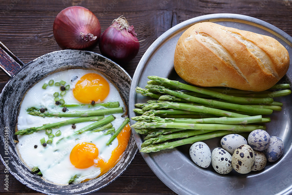 Country breakfast, fried eggs, bread, asparagus and onions on a wooden background