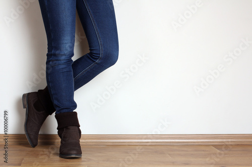 Young woman fashion legs in blue jeans and brown boots on wooden parquet floor on white background