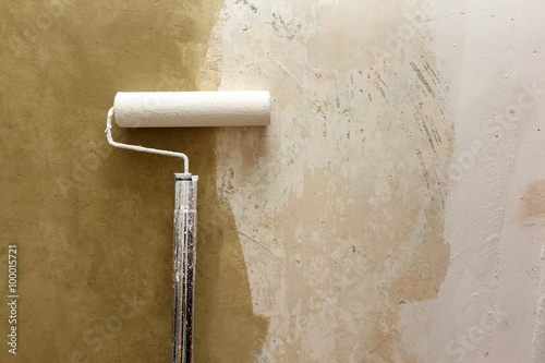 Paint roller applying paint on white wall, home improvements