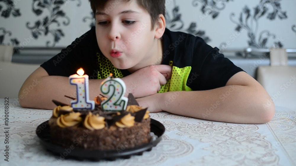 The boy blowing on  cake candles  with  number twelve