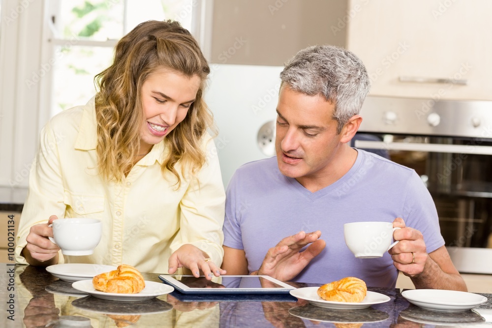 Happy couple using tablet and having breakfast