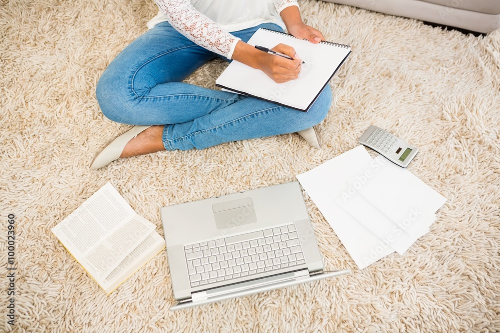 Fototapeta premium Above view of a woman writing note while using her laptop