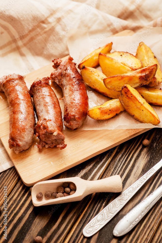 meat with vegetables , fried homemade sausage with roasted potatoes with garlic and pepper on a wooden background