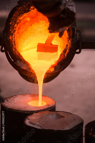 Foundry worker pouring hot metal into cast photo