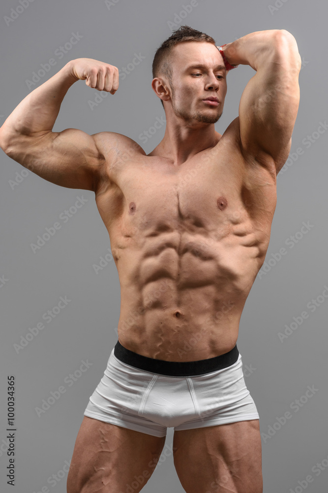 Shittless athletic man looking at the side and posing over grey background in white underwear