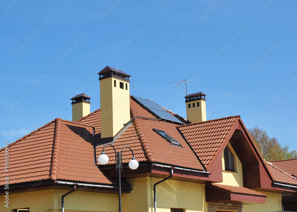Closeup of solar panel on red tiled house roof with skylights, chimney and roof window.
