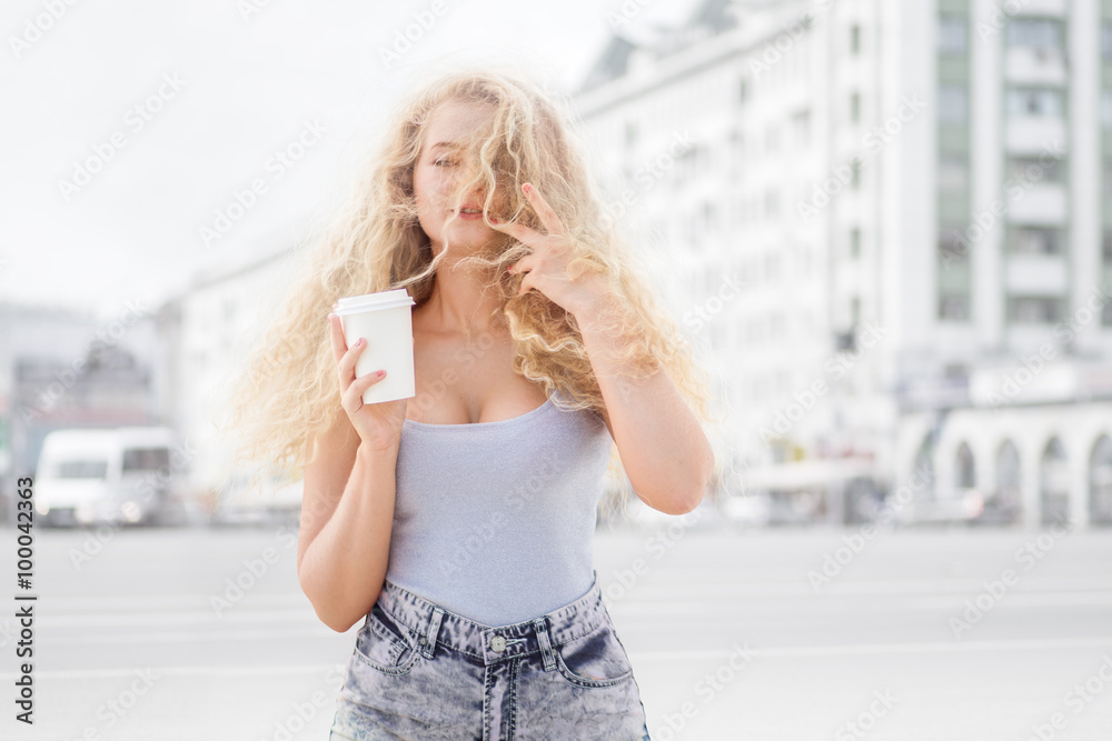 Happy smile / Happy young woman with long curly hair, holding a take away coffee cup and smiling with flirt in front of a camera against urban city traffic background. Happy smile / Happy young woman with long curly hair, holding a take away coffee cup and smiling with flirt in front of a camera against urban city traffic background.