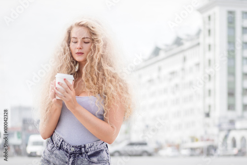 Happy smile / Happy young woman with long curly hair, holding a take away coffee cup and smiling with flirt in front of a camera against urban city traffic background.