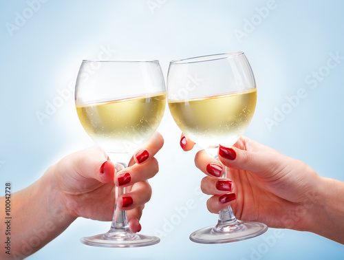 Two female hands toasting with white wine on blue background, close up