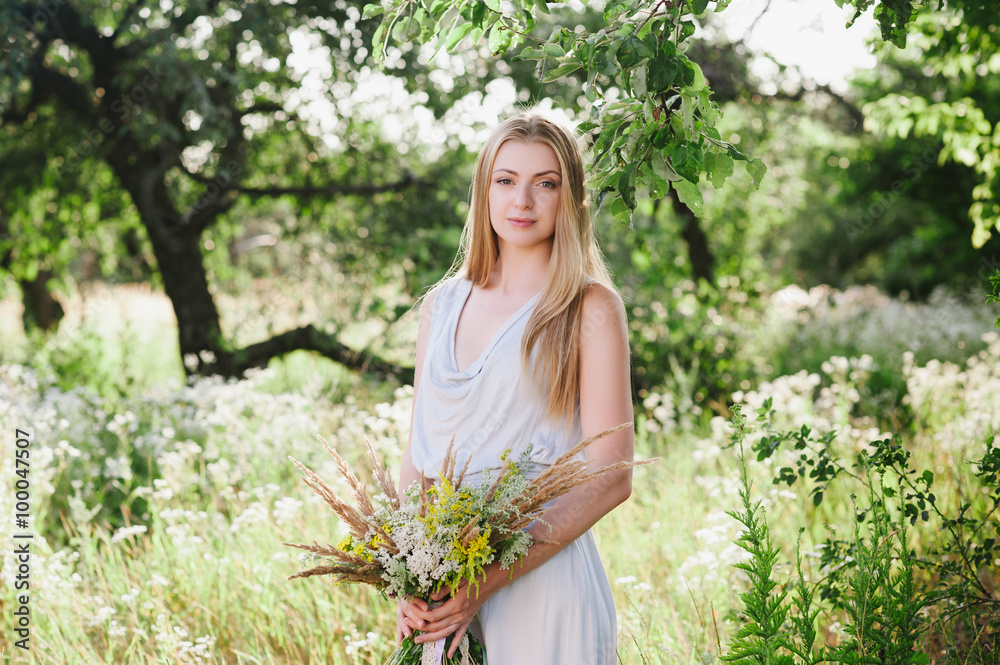 The beautiful blonde with long hair on nature with a bouquet of flowers The beautiful blonde with long hair on nature with a bouquet of flowers